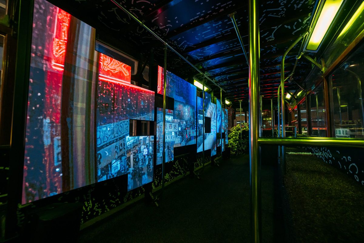 The upper deck at night, its windows replaced by large screens showing red and blue city images.